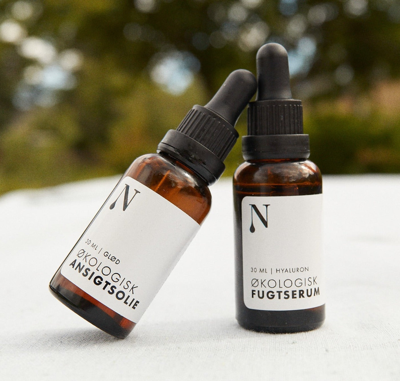 Ansigtsolie Glød og Fugtserum i brune dropperflasker liggende i sne