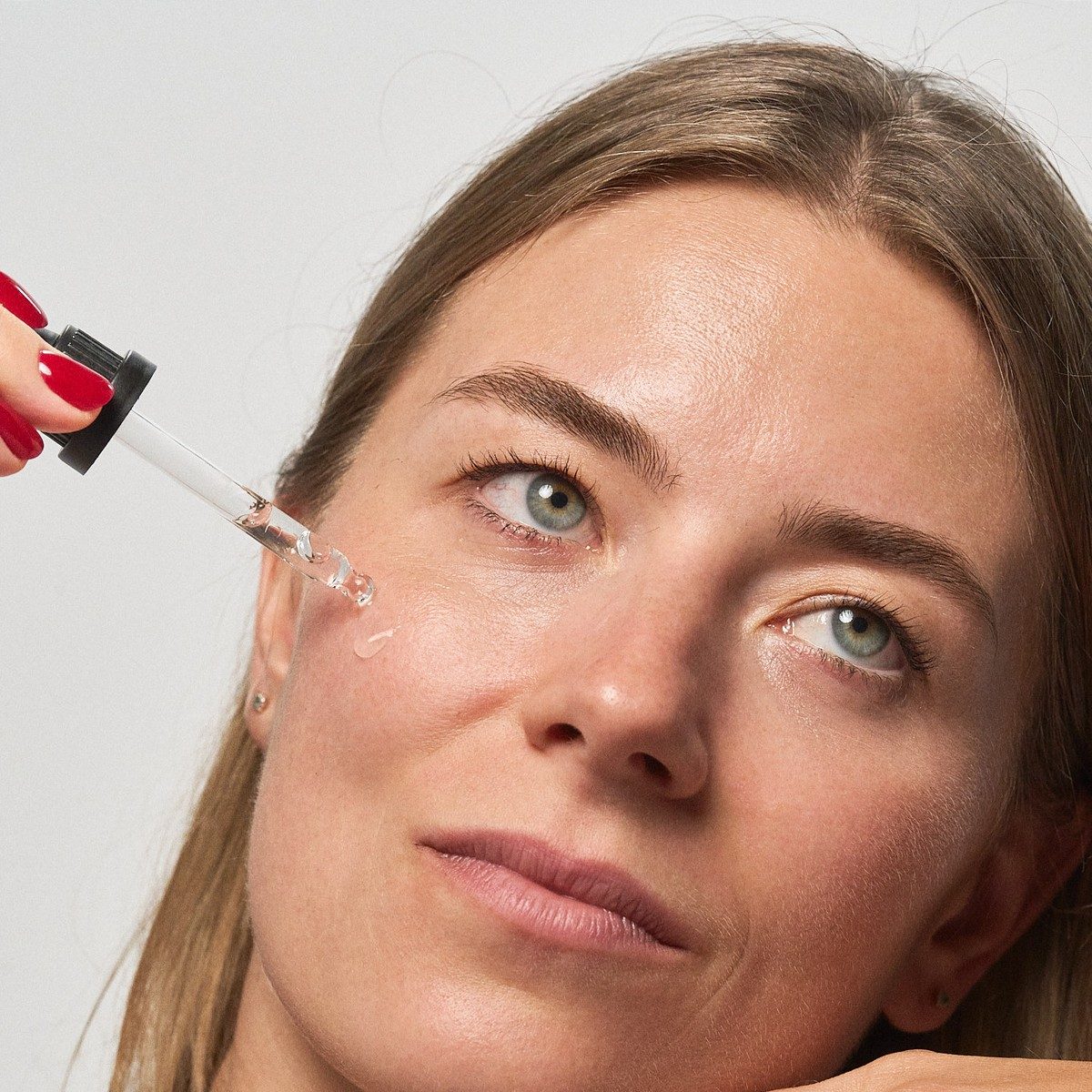 Kvinde drypper klart fugtserum på kindbenet med pipetten