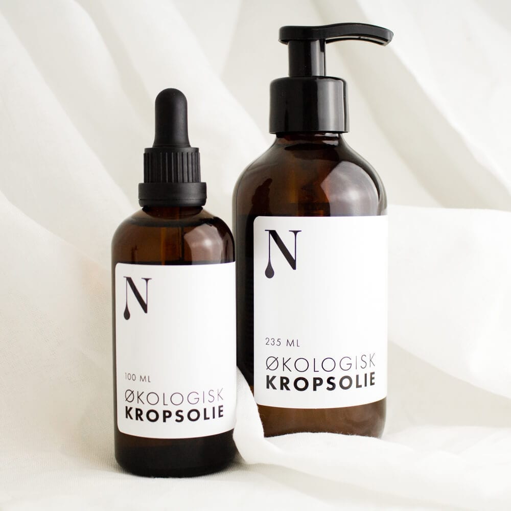 To brune glasflasker med økologisk kropsolie, 100 ml med pipette og 235 ml med pumpe, på hvidt stof
