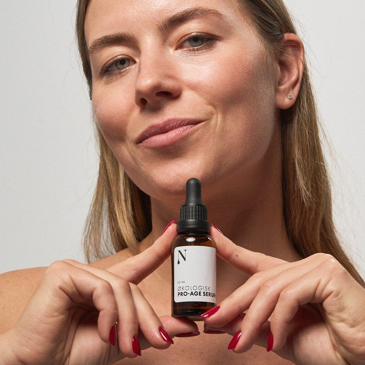 Kvinde holder Økologisk Pro-Age Serum frem mellem fingrene
