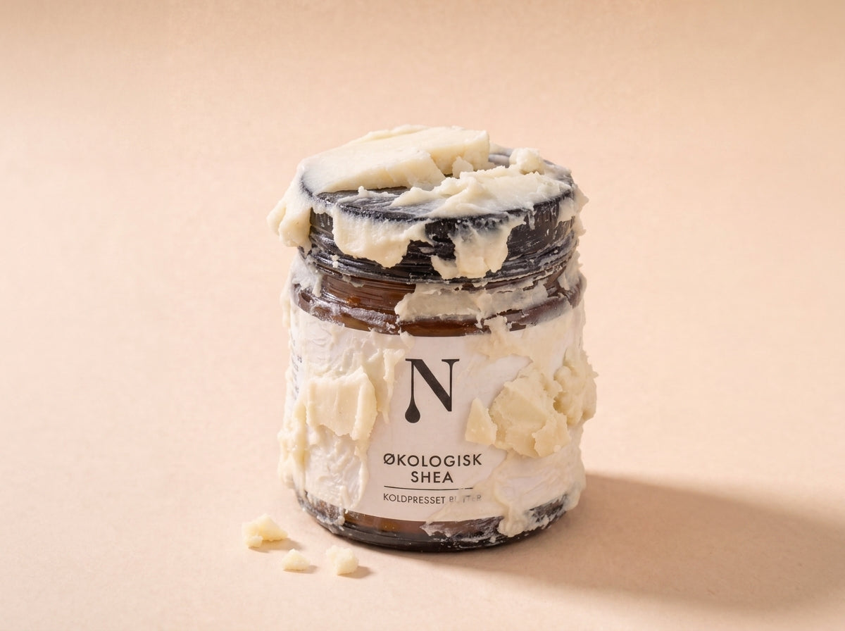 Naturligolie Sheasmør i krukke dækket af tykke klumper fast, elfenbensfarvet smør