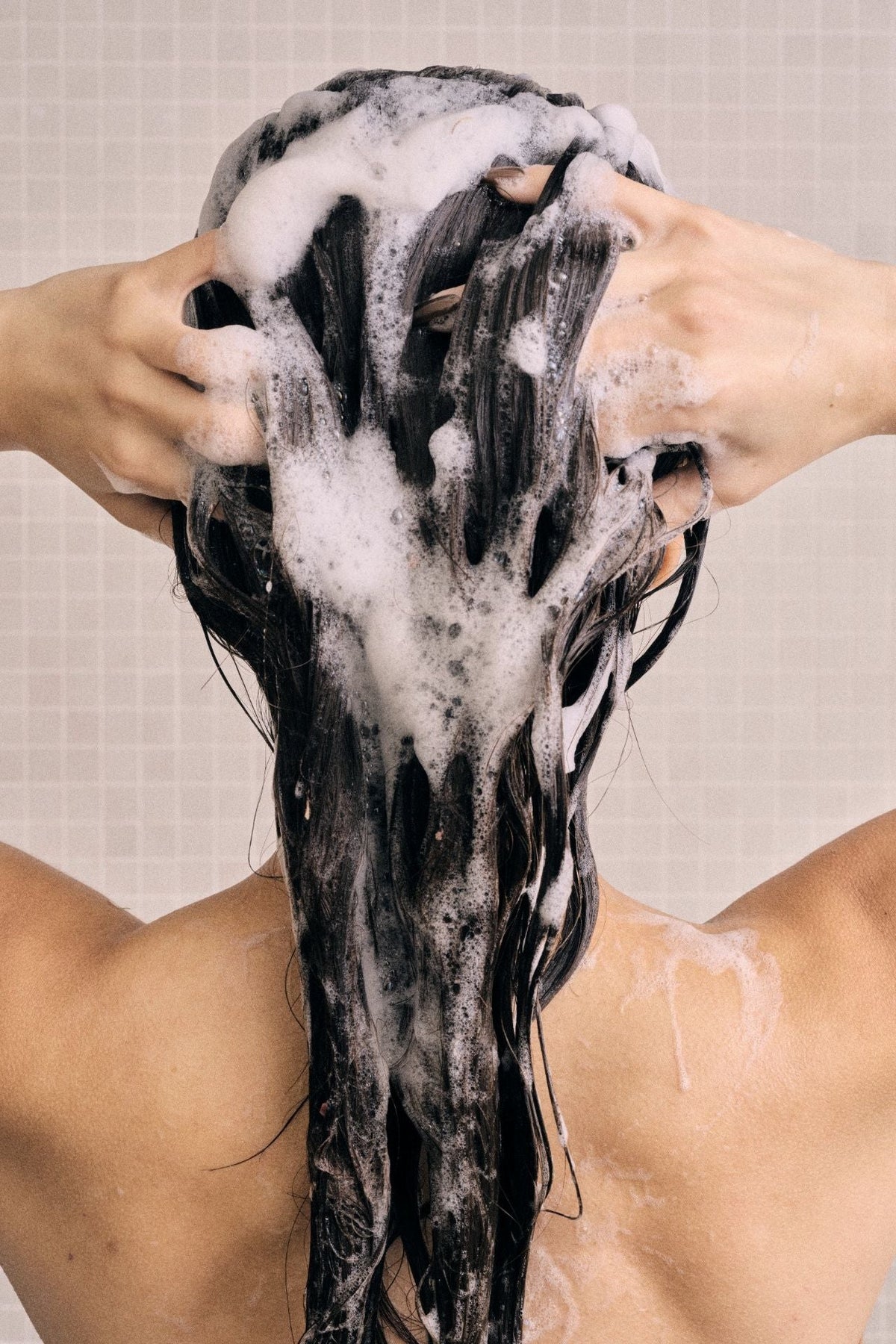 Kvinde set bagfra, der masserer shampoo ind i hovedbunden med begge hænder.