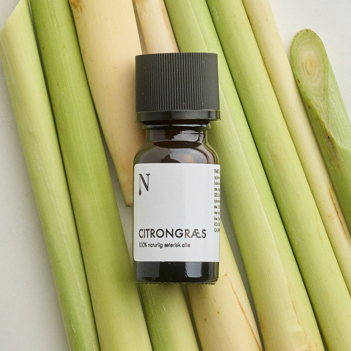 Flaske med citrongræsolie på stængler af citrongræs