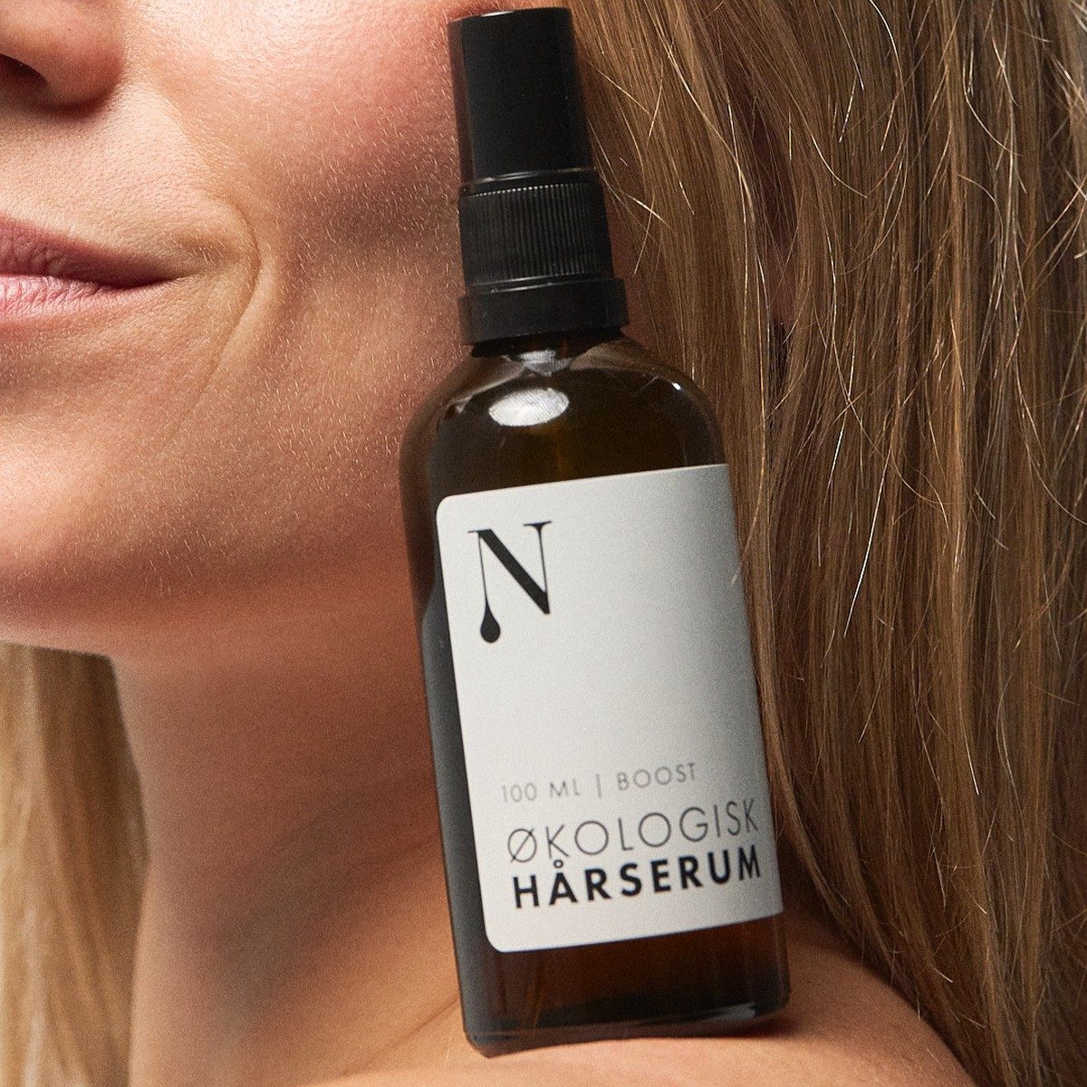 Kvinde holder Økologisk Hårserum 100 ml op ved kinden