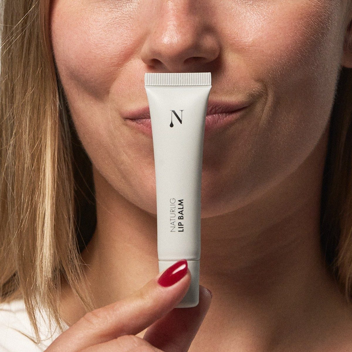 Kvinde holder Naturlig Lip Balm i lys tube op foran munden