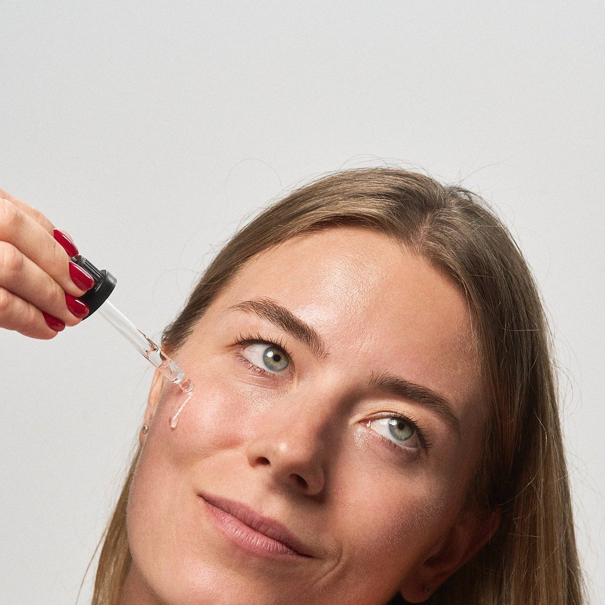 Kvinde smiler og drypper klart serum på kinden med pipetten