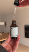 Kvinde fortæller om ingredienserne i Naturligolie Pro-Age Serum og drypper serummet på hånden