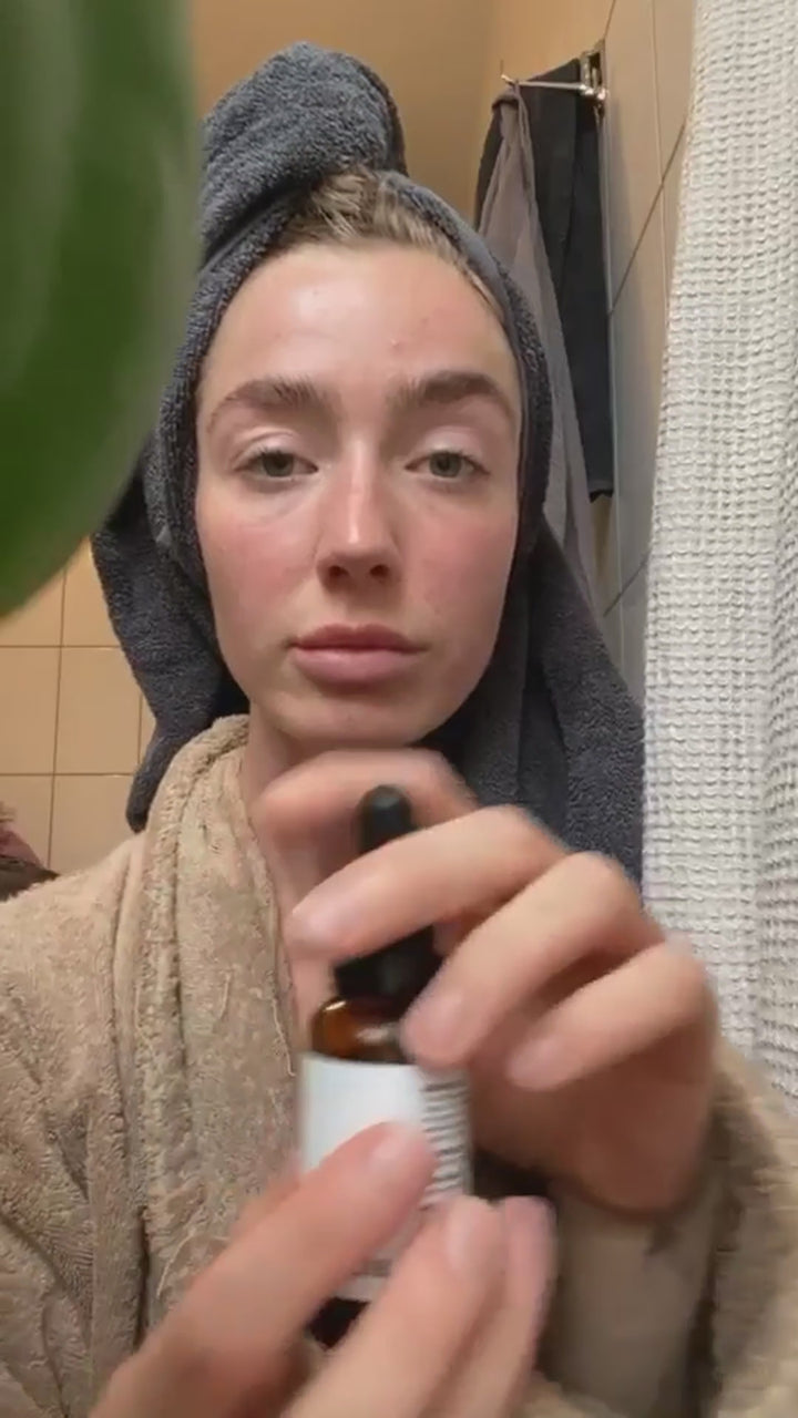 Kvinde i badekåbe drypper Ansigtsolie Glød i håndfladen og presser olien ind i ansigtet